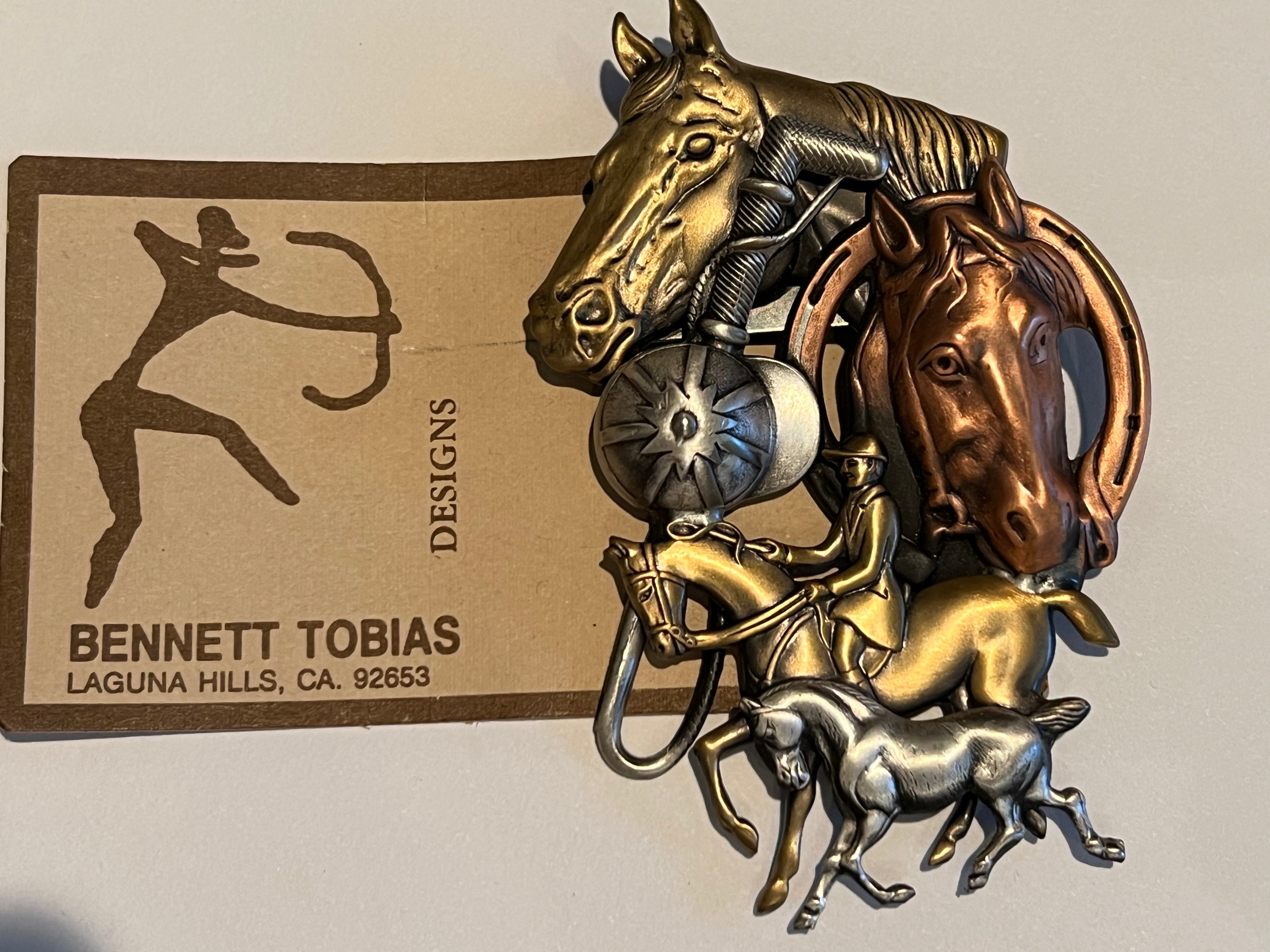 Bronze or brass sculpture of two horse heads and a rider on a horse and a foal trotting beside. Bennett Tobias Designs branding in the background. 